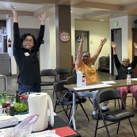 Residentes mayores de Oaks on Florence realizan ejercicios de estiramiento como parte de una clase de nutrición y bienestar impartida por CalFresh Healthy Living, UCCE Los Ángeles. La iniciativa promueve hábitos saludables a través de actividades prácticas y educación culturalmente relevante.