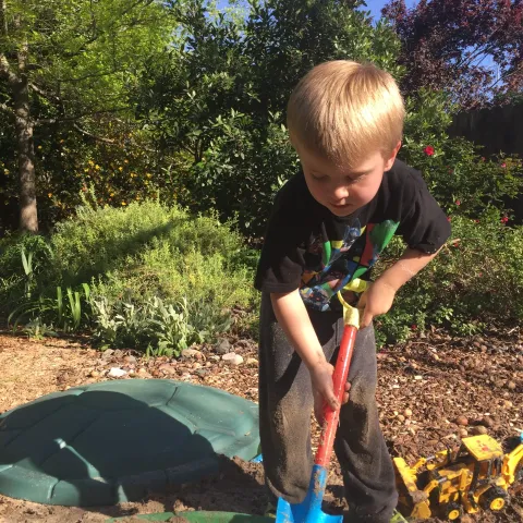 little blonde boy digging in with a shovel