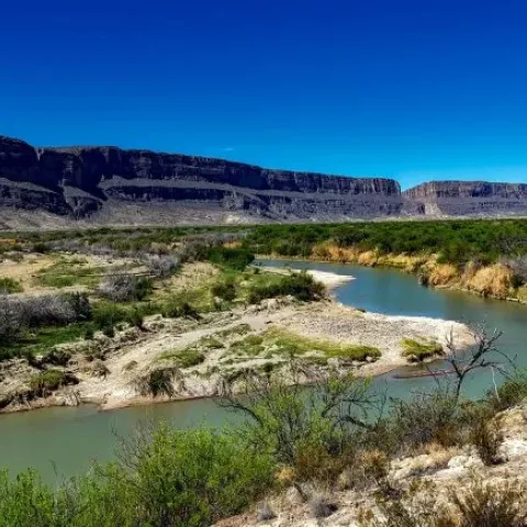 The Rio Grande River winds through a desert landscape with green shrubs