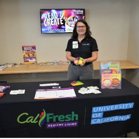 Lori stands behind a table displaying CalFresh Healthy Living University of California recipes and other handouts