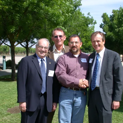Four men standing on grass surrounded by trees