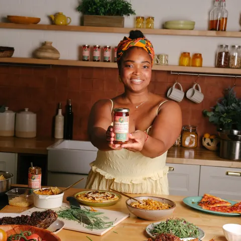Gloria Allorbi stands in a kitchen holding a bottle of Ghanaian vegan chili oil