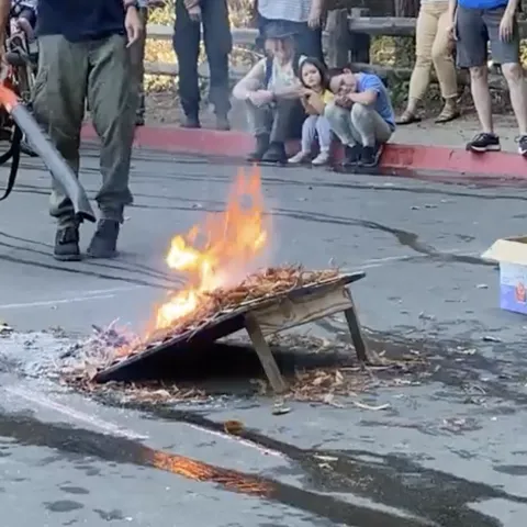 Leafblower simulates wind fanning flames as people watch it burn