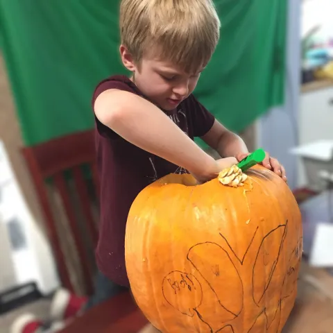blonde boy carving out a pumpkin