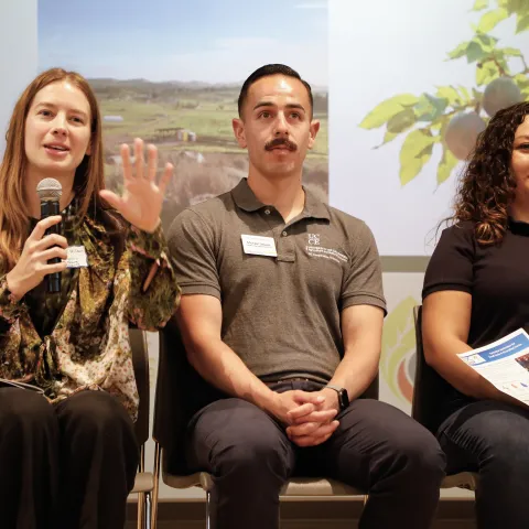 Three people sit on stage in front of a screen, speaking to an audience