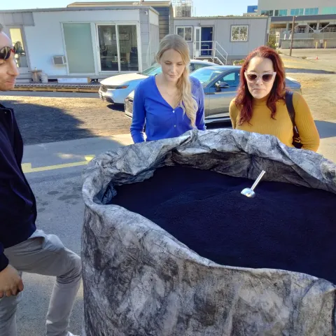 Three people standing next to an open Supersack of black OurCarbon biochar