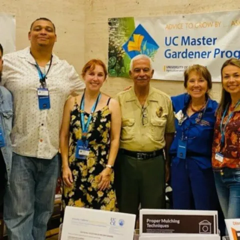 UC Master Gardener standing happily in a education booth display at a county fair, surrounded by learning material. 