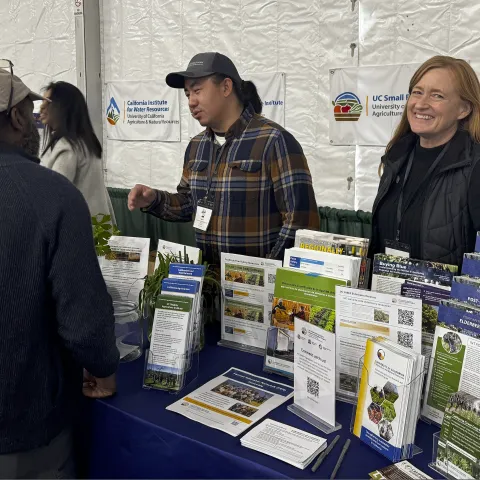 Two people and a participant at the UC ANR Organic Agriculture booth during Ecofarm 2026.