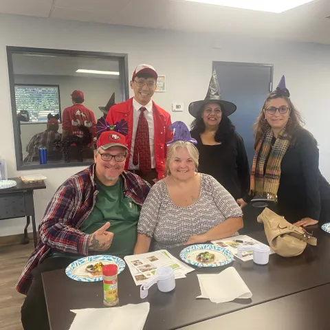 Burkes smile at a table during an EFNEP class as Danny Vang stands behind them, alongside other course participants wearing Halloween costumes