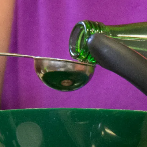Hands pouring a liquid from a bottle into a small measuring spoon