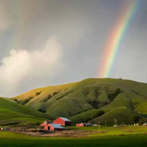 rainbow touching down on rolling green hills and a red barn