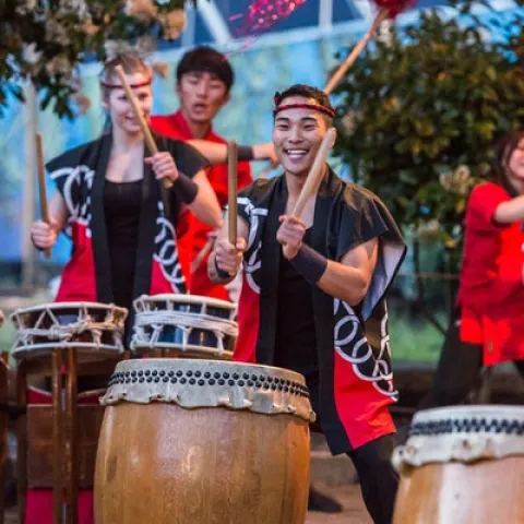 Young people dressed in black and red drumming on Japanese drums.