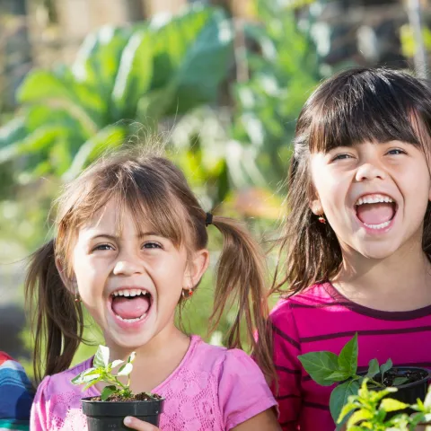 Four young children smile holding potted plants.