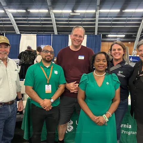 Six people stand in a row. A man and a woman are wearing 4-H green