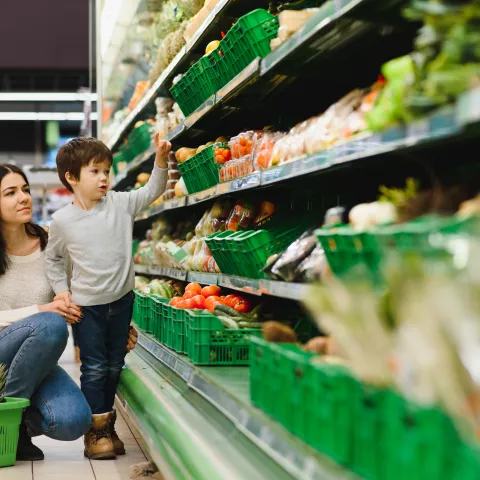 Mother and son shopping in the produce section of a grocery store.