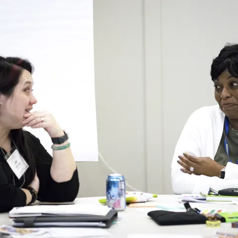 Jaki Hsieh Wojan and Tina Jordan sit at a table having a ocnversation.
