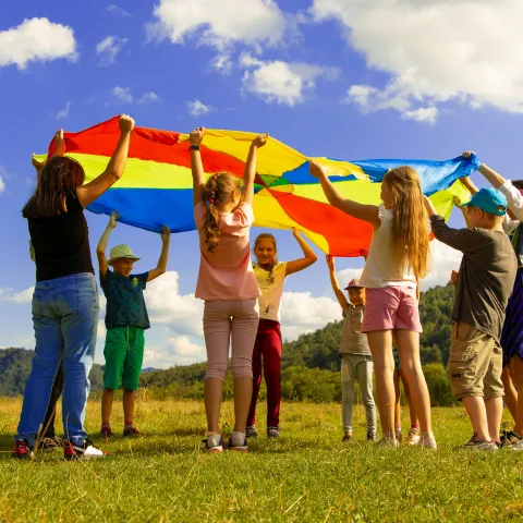 A group of children play outside with a parachute