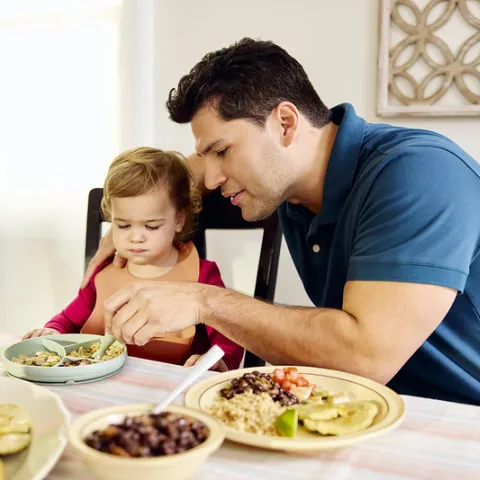 A father helps his infant eat dinner.