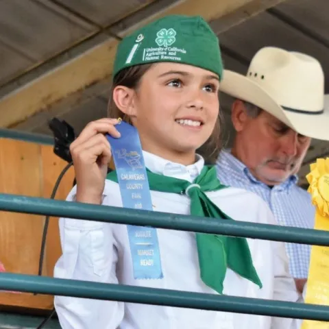 Girl in 4-H uniform holding blue and yellow ribbons at the fair