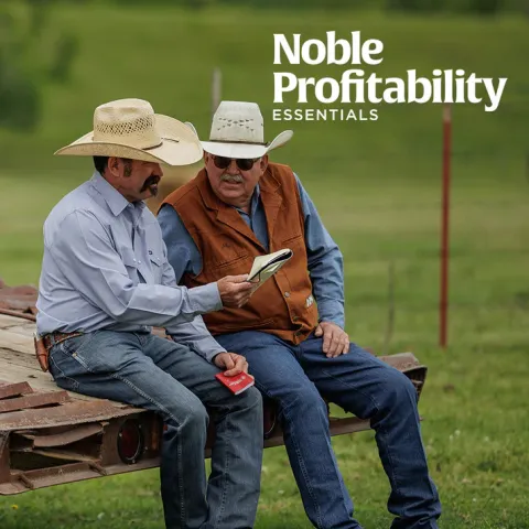 Two ranchers sitting side by side looking at a magazine document