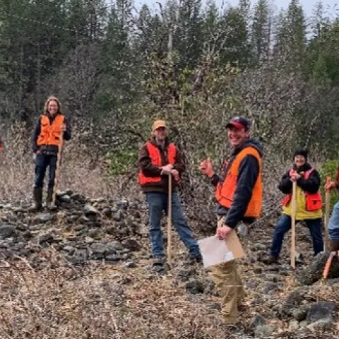 Participants wearing forestry vests stand together in a forest. 