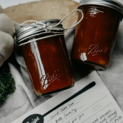 two ball mason jars containing carrot cake jam tied with twine sitting on top of a printed recipe page