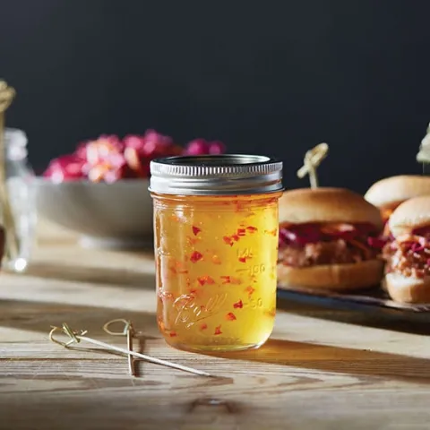 a glass jar of red pepper jelly in front of pork sliders