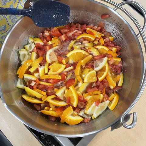 a pot of ingredients used to make tomato marmalade including cut tomotoes and citrus