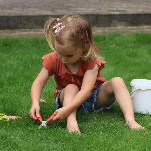 Photo of young child sitting on grass, cutting it with children's scissors. (Marjon Besteman on Pixabay)