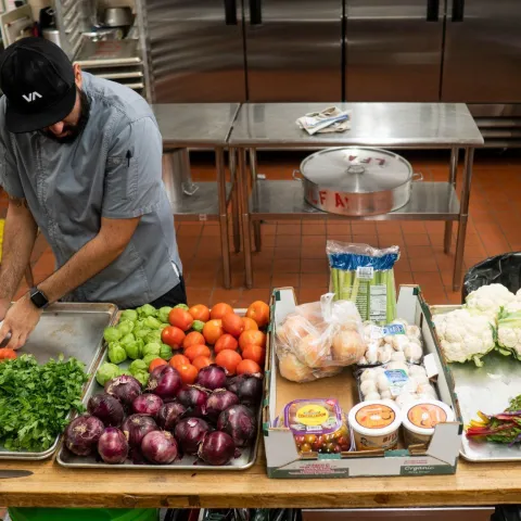 Chef stands behind a table with prepared food in a commercial kitchen.