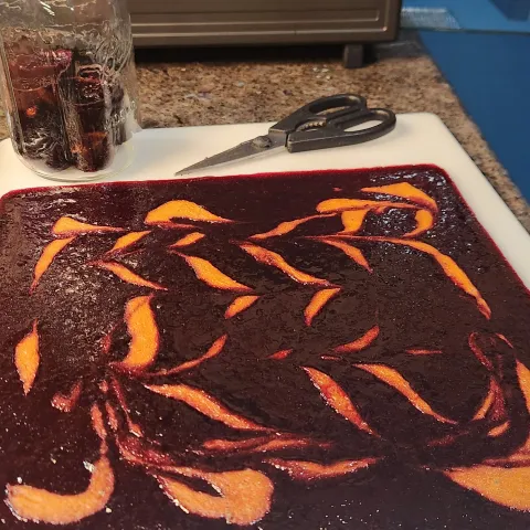 a rectangle of dehydrated berry and apricot puree on a cutting board next to a pair of scissors