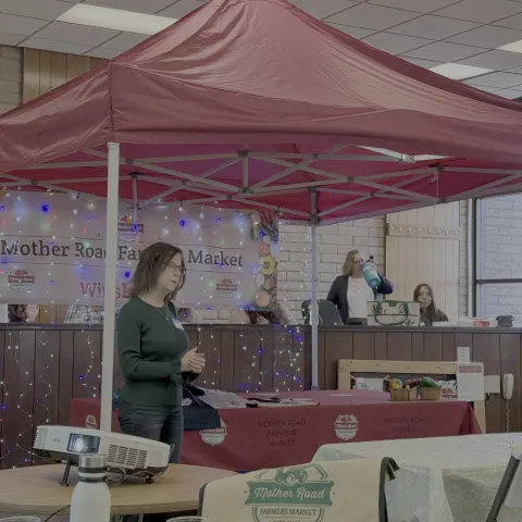 Food business client standing at their stall under a tent.