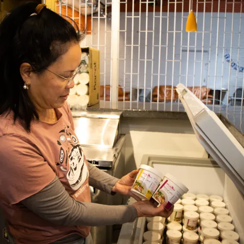 Owner of Pink Elephant Kitchen standing with products next to a freezer