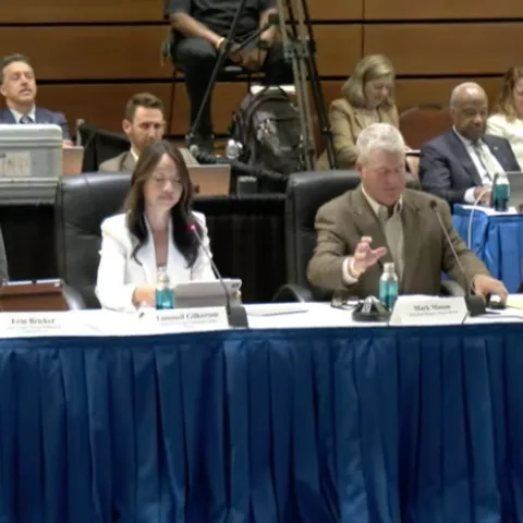 Four people sitting at a long table with audience behind them.