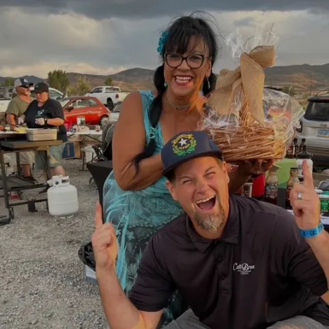 Two people standing at an outdoor market location. One is holding a wrapped basket of goods.