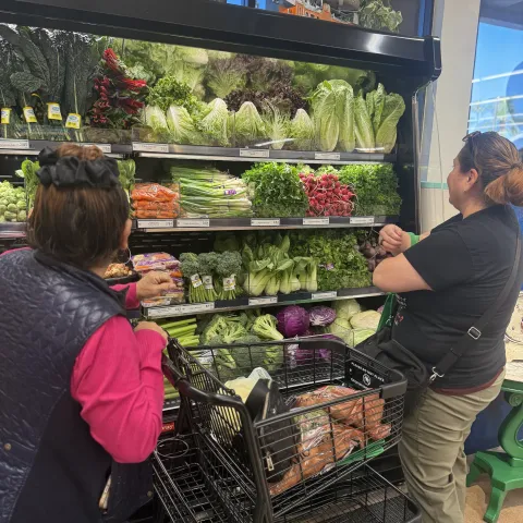 Two people standing next two a produce shelf