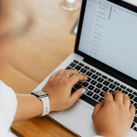 A woman with blue fingernail polish types on a laptop.