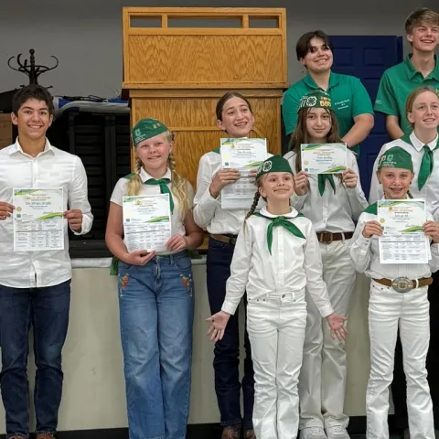4-H members stand in front of a stage with their public speaking contest awards.