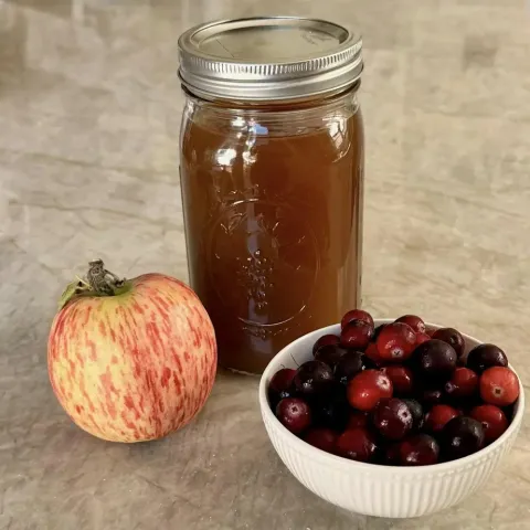 An apple and bowl of cranberries next to a jar of juice.
