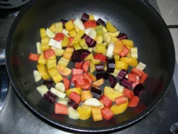A frying pan filled with diced orange, purple, and white carrots being cooked.