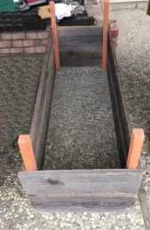 An empty raised bed showing final construction with gopher wire at the bottom, sturdy posts at the corners, and wooden sides