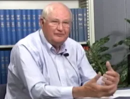 Jim Clawson sitting in front of a bookcase and a potted plant.