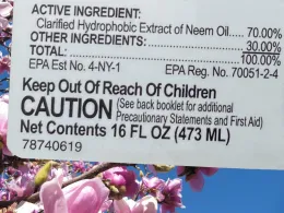 A room oil product label detailing ingredients, safety instructions, and caution warnings, set against a backdrop of pink peach blossoms.