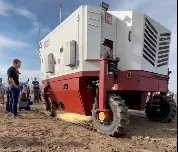 Machine in field emits laser beam onto weeds in soil.