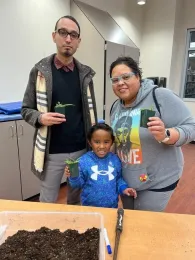 Family of three with little boy smiling and holding his potted plant.