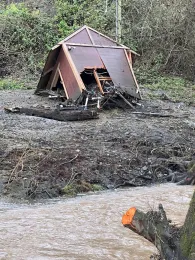 Broken wooden house lays on its side on the creek bank.