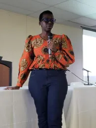 Woman wearing an orange print blouse speaks into a handheld mic.