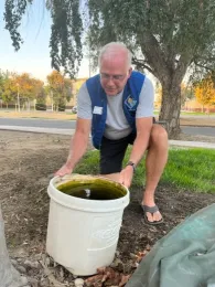 Man crouching beside white bucket to examine contents.