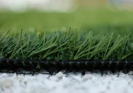 Close-up of artificial turf with vibrant green blades and a dark backing, resting on white gravel.