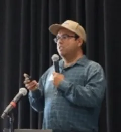 Man in a baseball hat speaks into mic